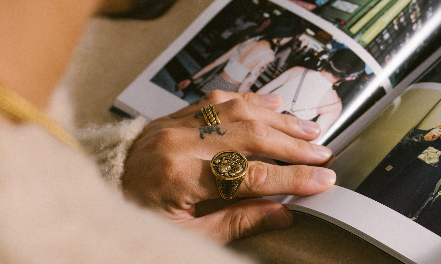 Man flicking through a jewelry style guide book. He's wearing bold gold signet rings