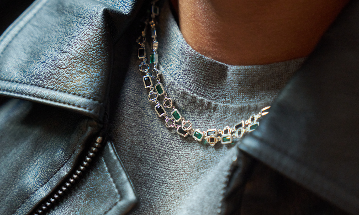 Close up of two men's silver gemstone necklaces worn over a grey crew neck t-shirt