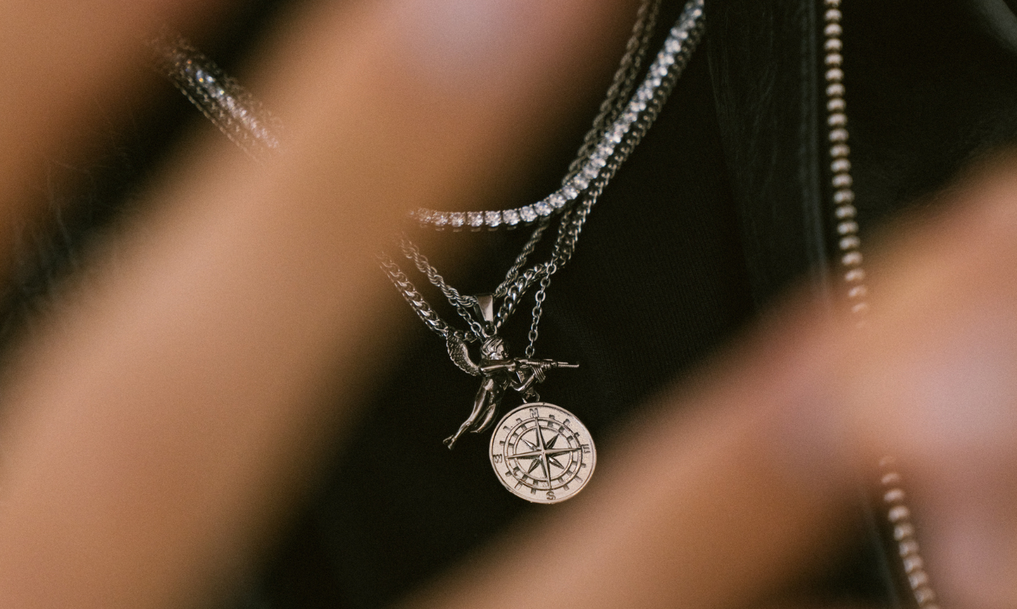 Close up shot of man's chest wearing a plain black t-shirt and silver jewelry including necklaces and chains