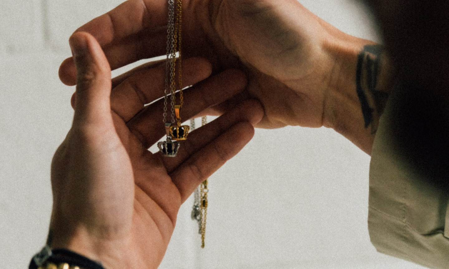 Close up of a man holding two crown Pendants Necklaces. One gold, one silver, both set with black onyx stones. The highest quality and most durable jewelry for men. 