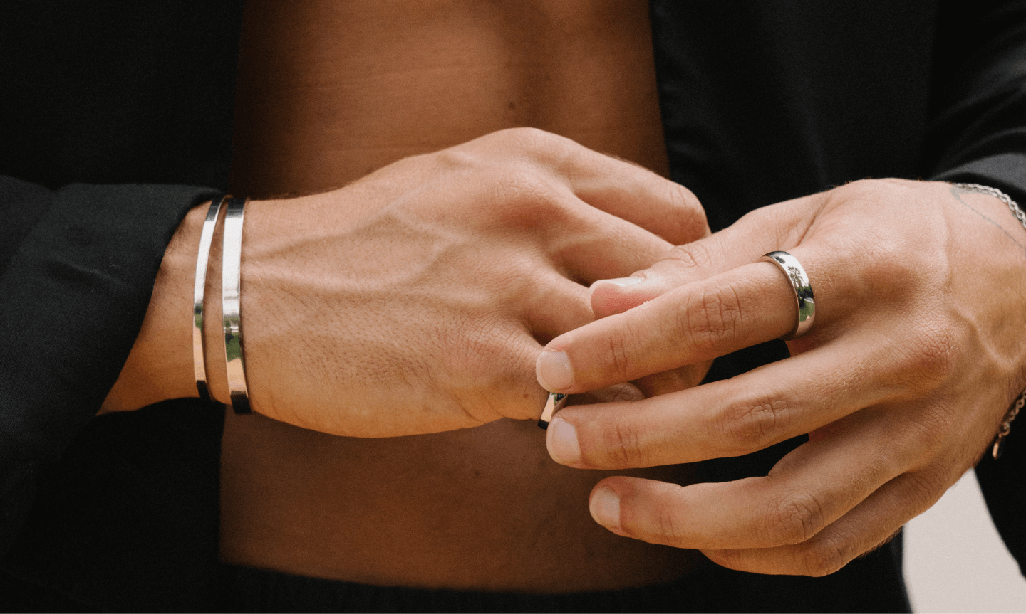 Man wearing simple men's jewelry including a minimal silver cuff bracelet and classic silver rings 