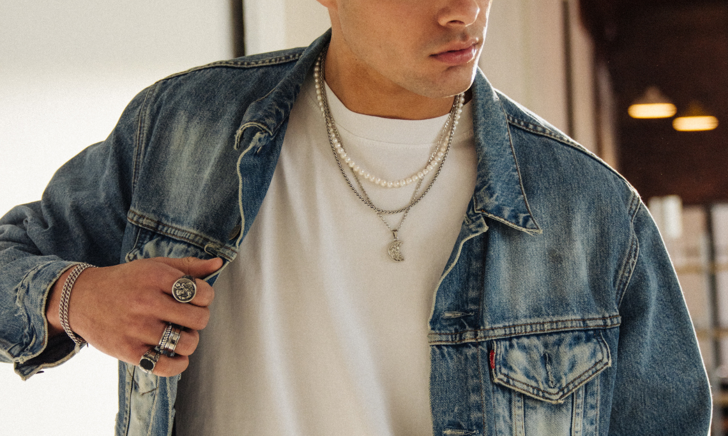 Man wearing a plain white t-shirt with a denim jacket and silver pendant necklaces and cuban link chains