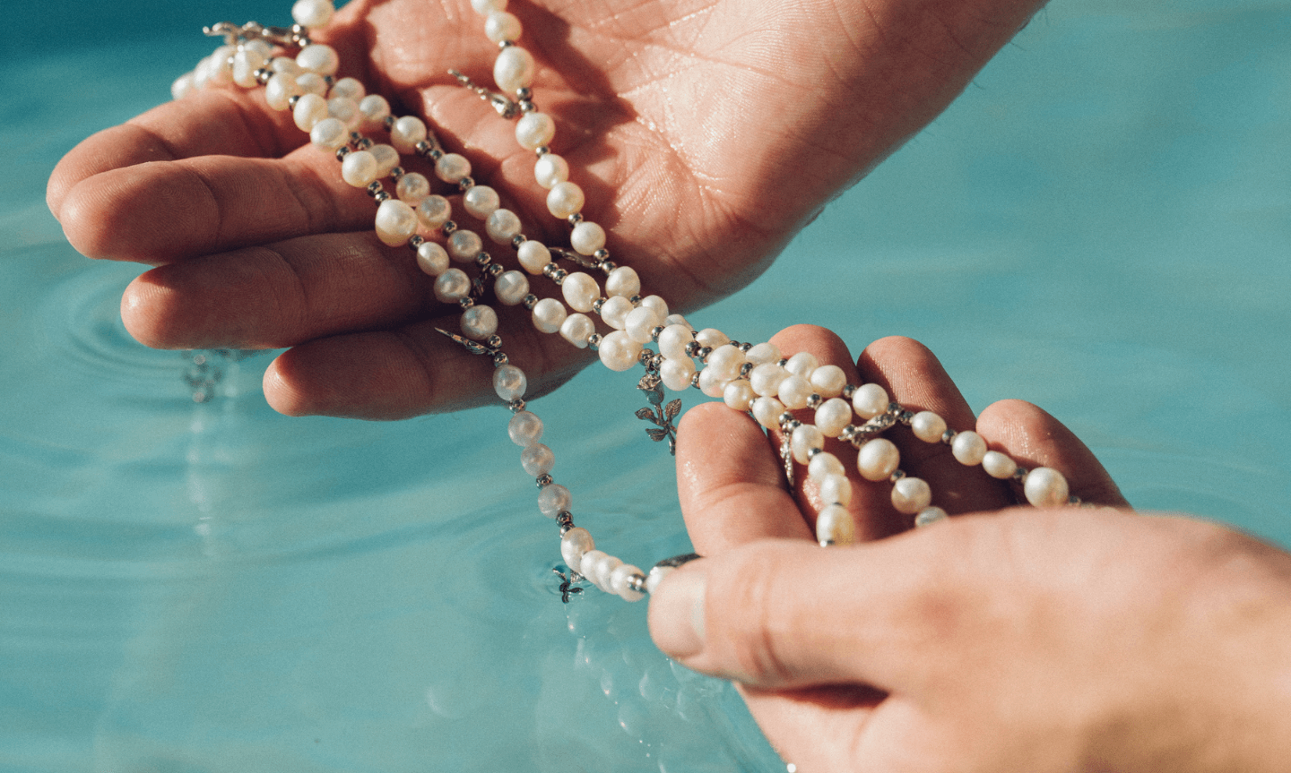 Man holding a men's Pearl Necklace and dipping it in water