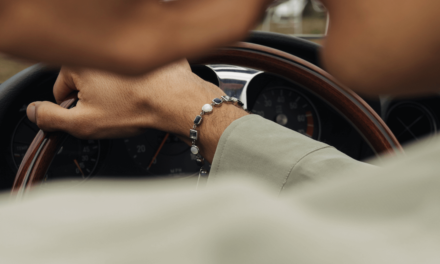 mans hand rest of a car steering wheel wearing a men's gemstone bracelet
