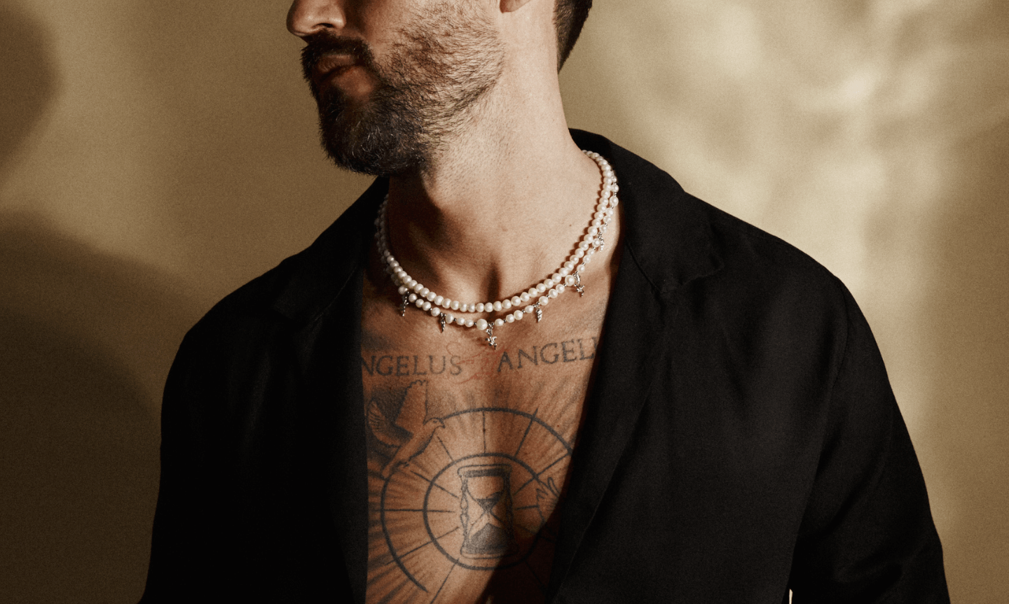 Man in an open collar black cuban shirt styling with two sets of mens pearl necklaces