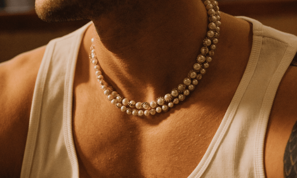 Man wearing a plain white vest with a shadow across his chest. He's styling two simple and real mens pearl necklaces 